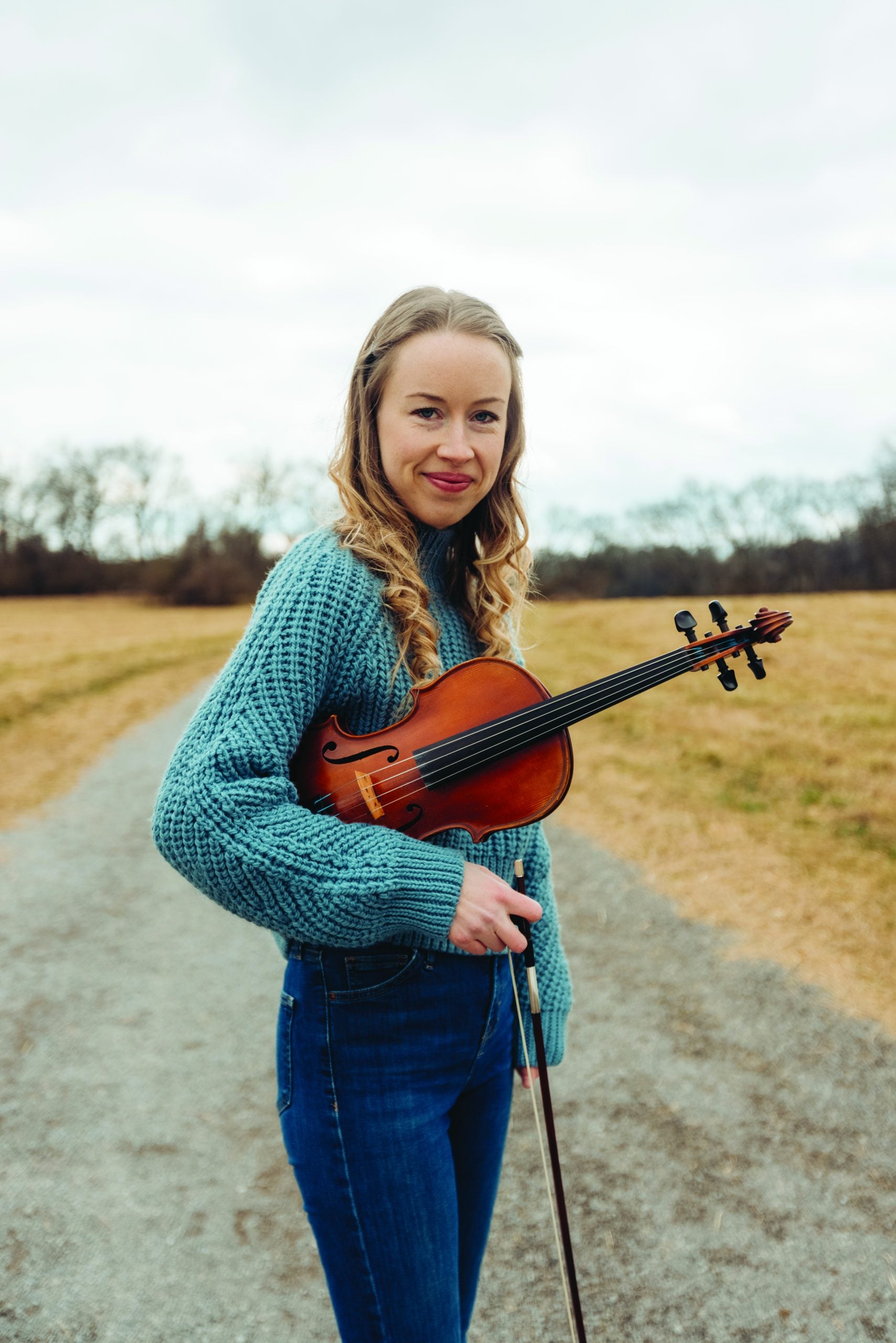 Bronwyn smiling for a photo and casually holding her fiddle.