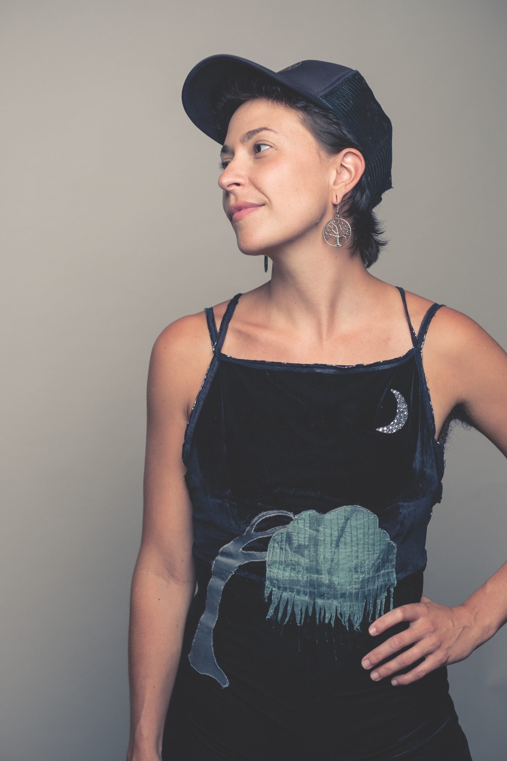 Lindsay Lou poses with her hand on her hip while wearing a black top and black ball cap.