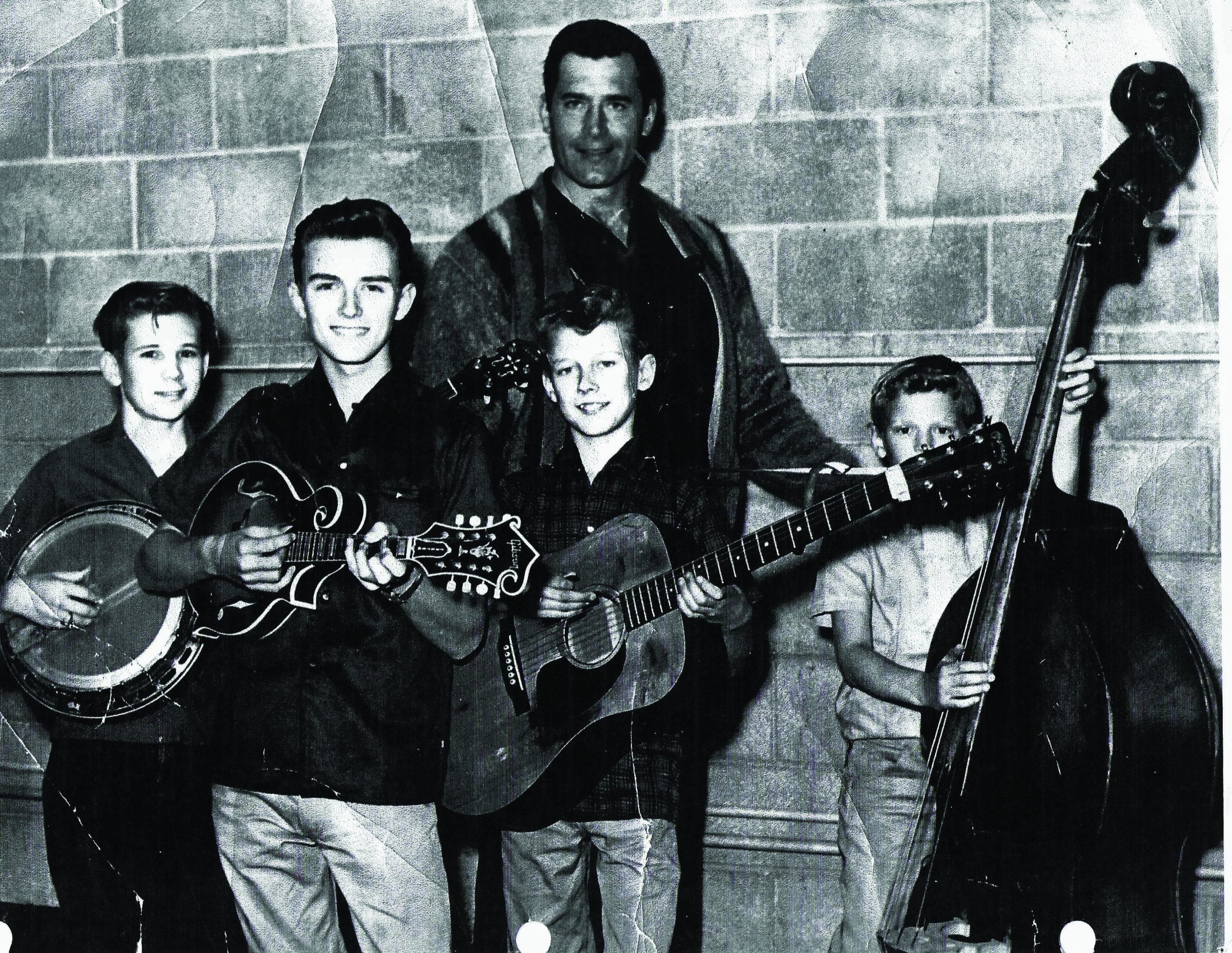 Larry Rice (mandolin), Tony Rice (guitar), and Ron Rice (bass) perform at the Grand Opening of a Harley-Davidson Motorcycle store in southern California in the early 1960s.  Andy Evans is on banjo.  The band is posing with actor Clint Walker, star of the television show Cheyenne.  