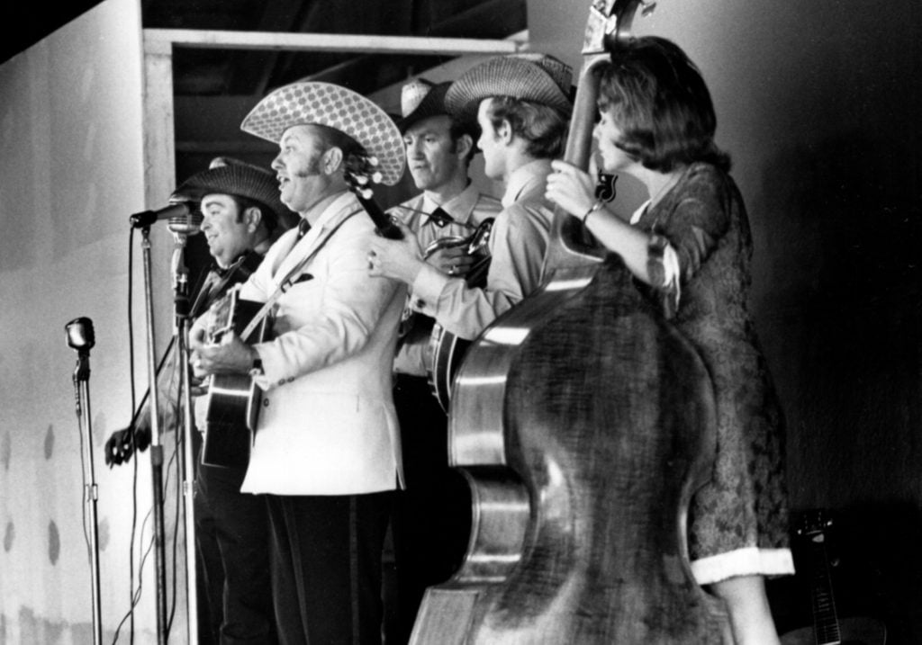 Jimmy Martin and the Sunny Mountain Boys perform at a country music park in Logan, Ohio, July 1969. Left to right: Vernon Derrick, Jimmy Martin, Doyle Lawson, Chris Warner, and Gloria Belle Flickinger. Photo by Carl Fleischhauer