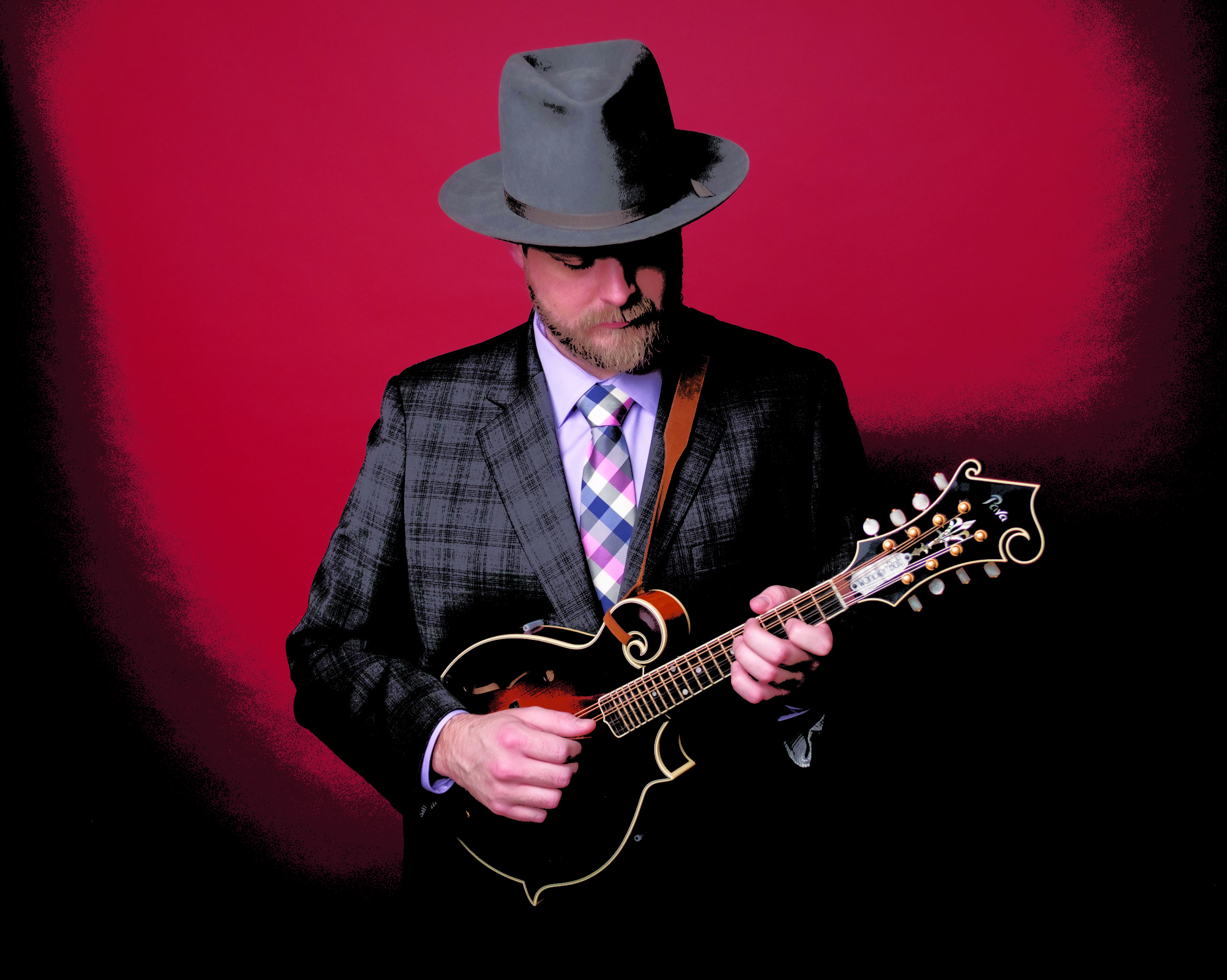 Nate Lee poses for a dramatic photo in a suit and tie in front of a red backdrop with his instrument