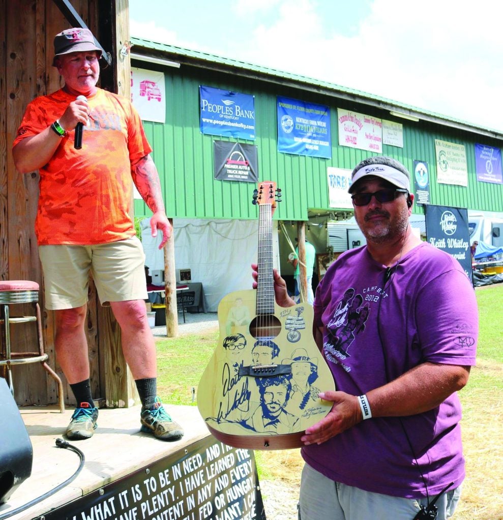 A guitar donated by Chris Keefe was auctioned at the festival to raise funds for Stormy Cushing, a young bluegrass fan who was injured in a car accident.  George Adams, Colt’s father, is on the stage and Vic Adams is holding the guitar. Photo by Angela MarxA guitar donated by Chris Keefe was auctioned at the festival to raise funds for Stormy Cushing, a young bluegrass fan who was injured in a car accident.  George Adams, Colt’s father, is on the stage and Vic Adams is holding the guitar. Photo by Angela Marx
