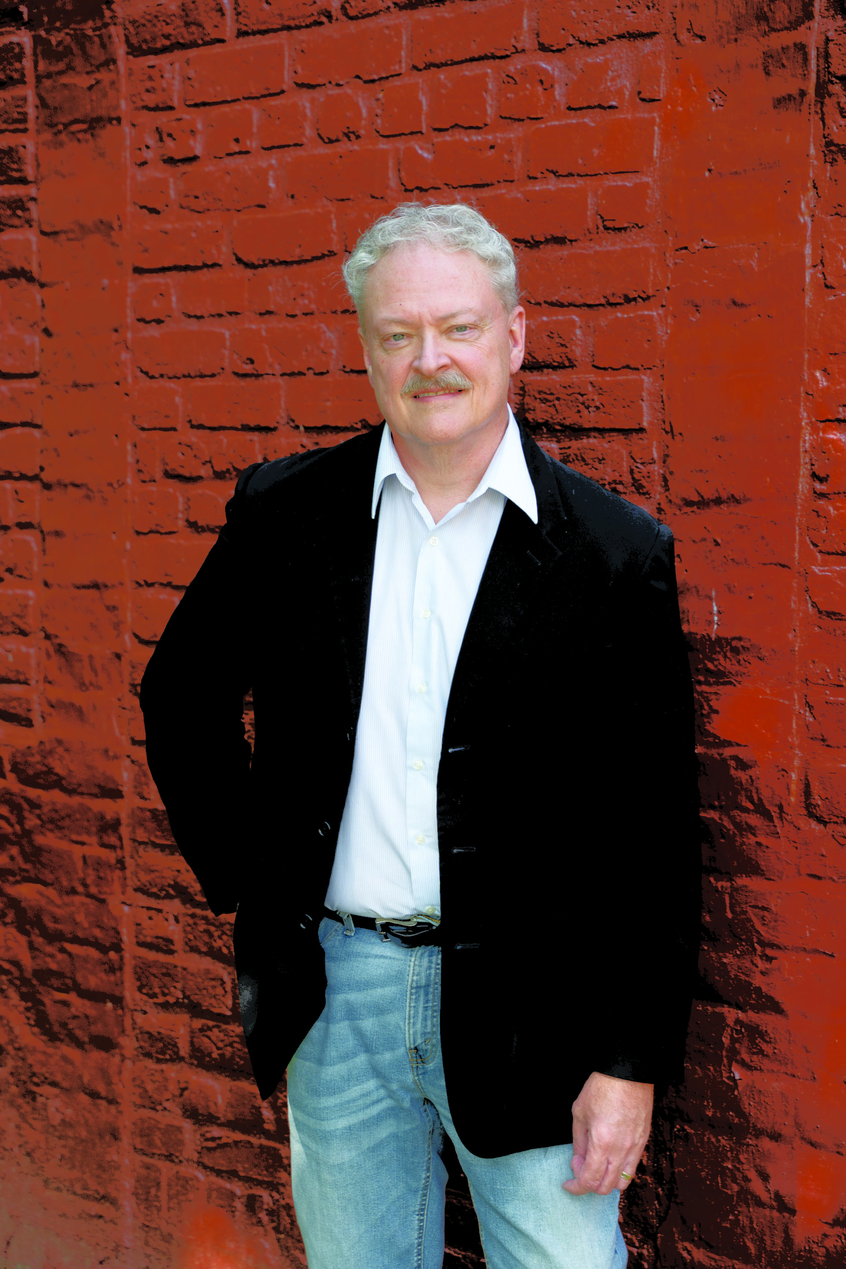 Tim Stafford poses for a picture against a red brick wall