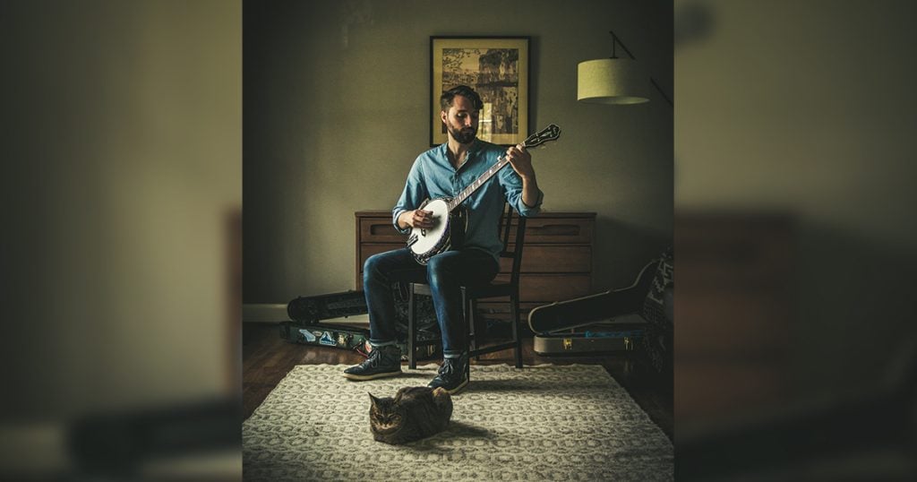 Wes Corbett playing his banjo in his living room with his cat