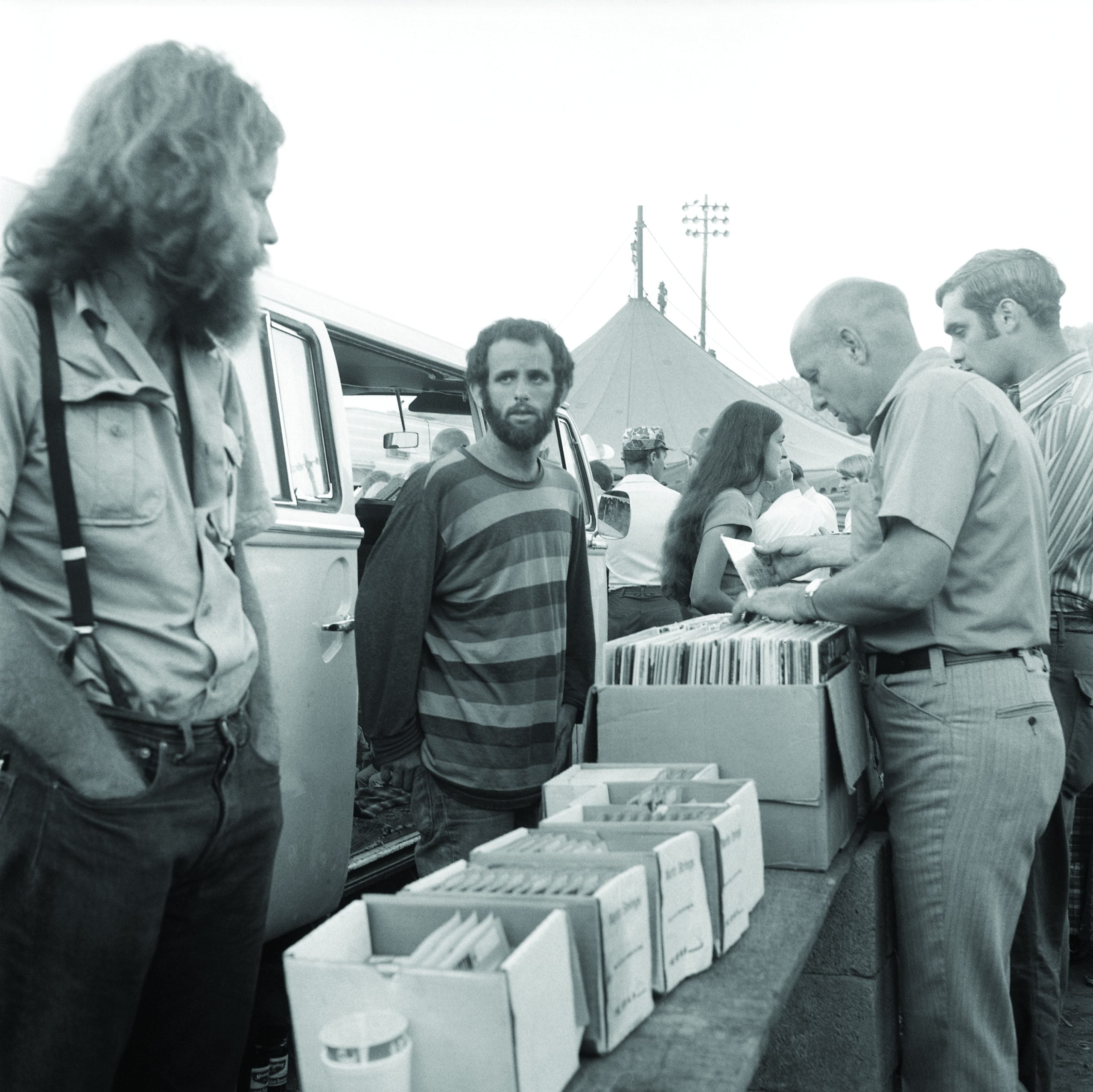 The three “Rounders” selling records at a festival out of their VW bus          