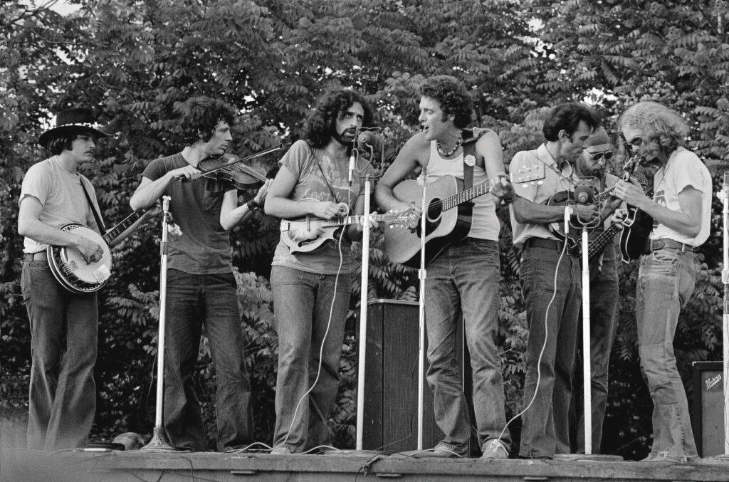 The Culpeper-Warrenton Bluegrass Festival in Warrenton, Virginia in 1973. (Left to Right) Butch Robins, John Hartford, David Grisman, Peter Rowan, Buck White, Ebo Walker and Sam Bush.  //  Photo by Phil Zimmerman Courtesy Of Bluegrass Music Hall Of Fame & Museum