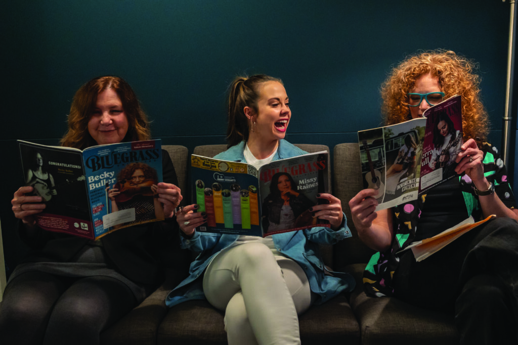 Missy Raines, Sierra Hull and Becky Buller reading each other’s cover stories in Bluegrass Unlimited Magazine. // Photo by Madison Thorn